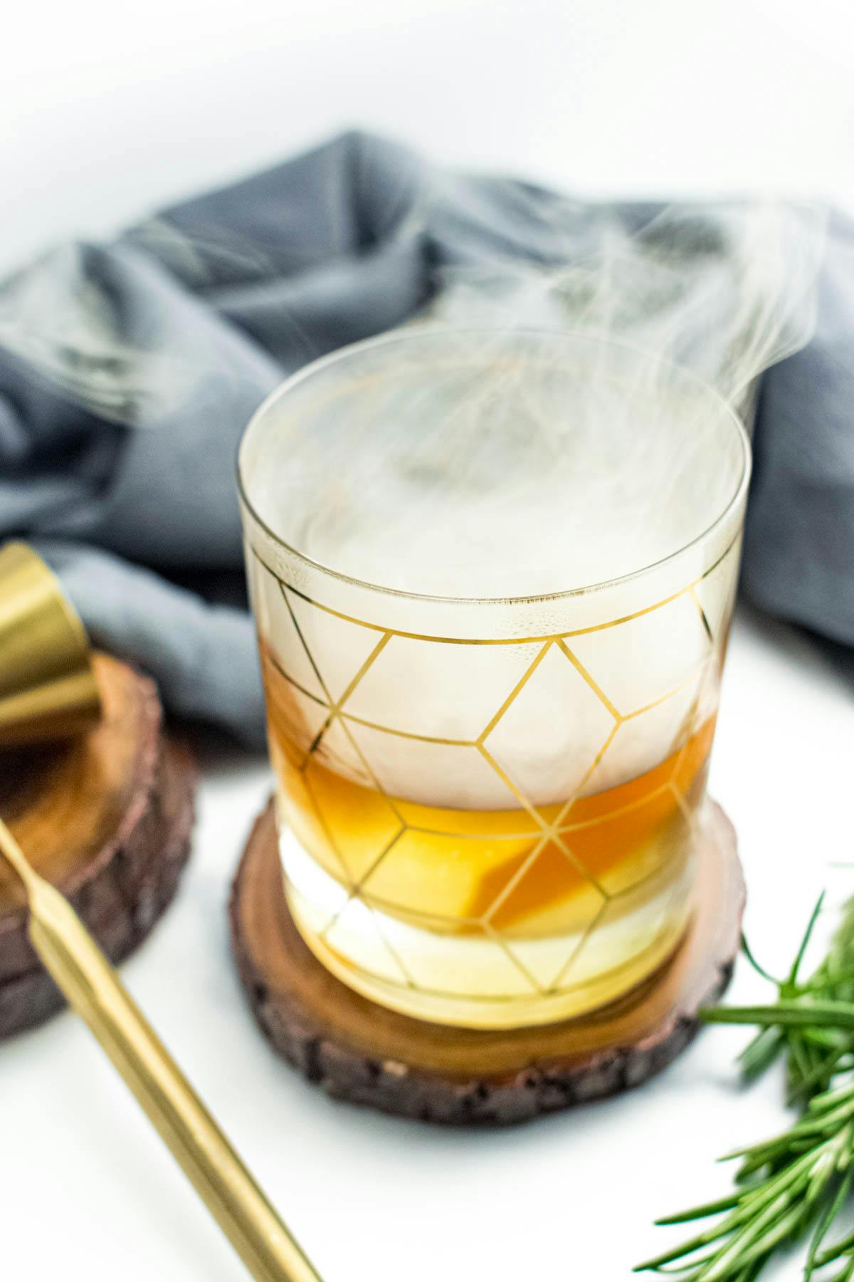 A smoking cocktail in a gold decorated rocks glass.