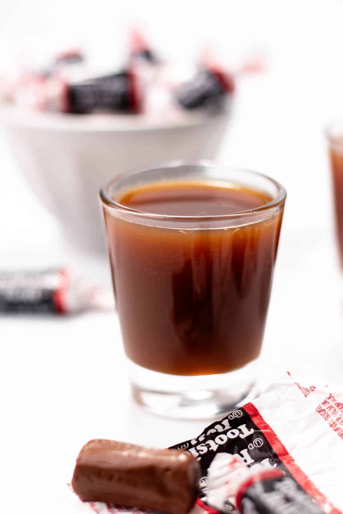 A shot glass of brown liquid sits near tootsie roll candies.