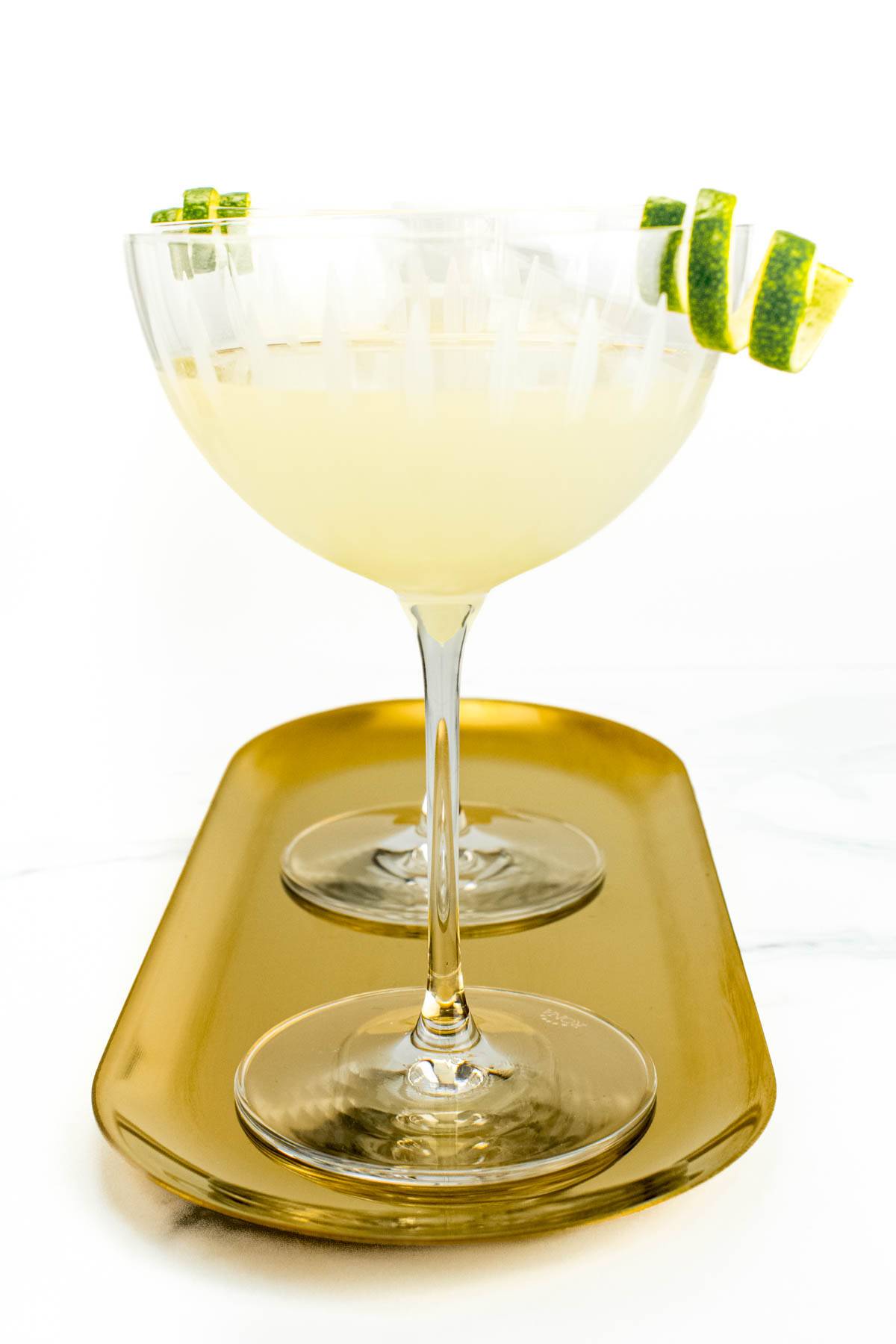 Two yellow cocktails sit on a gold oval tray.