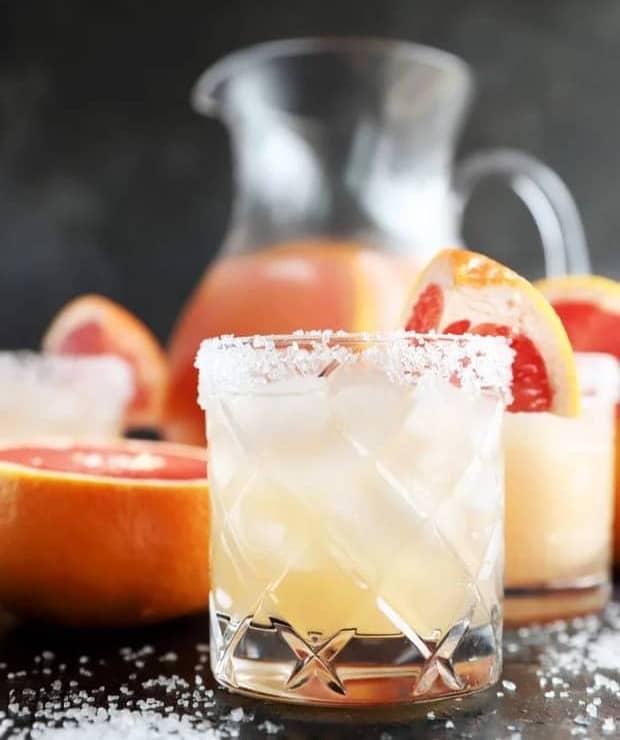 A pale drink with a salted rim sits near a pitcher of pale pink cocktails.