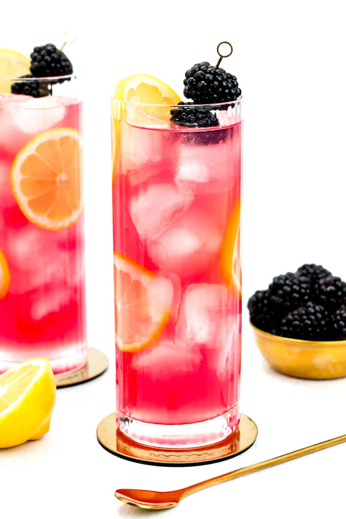 A bright pink drink sits near half a lemon and a gold bowl of blackberries.