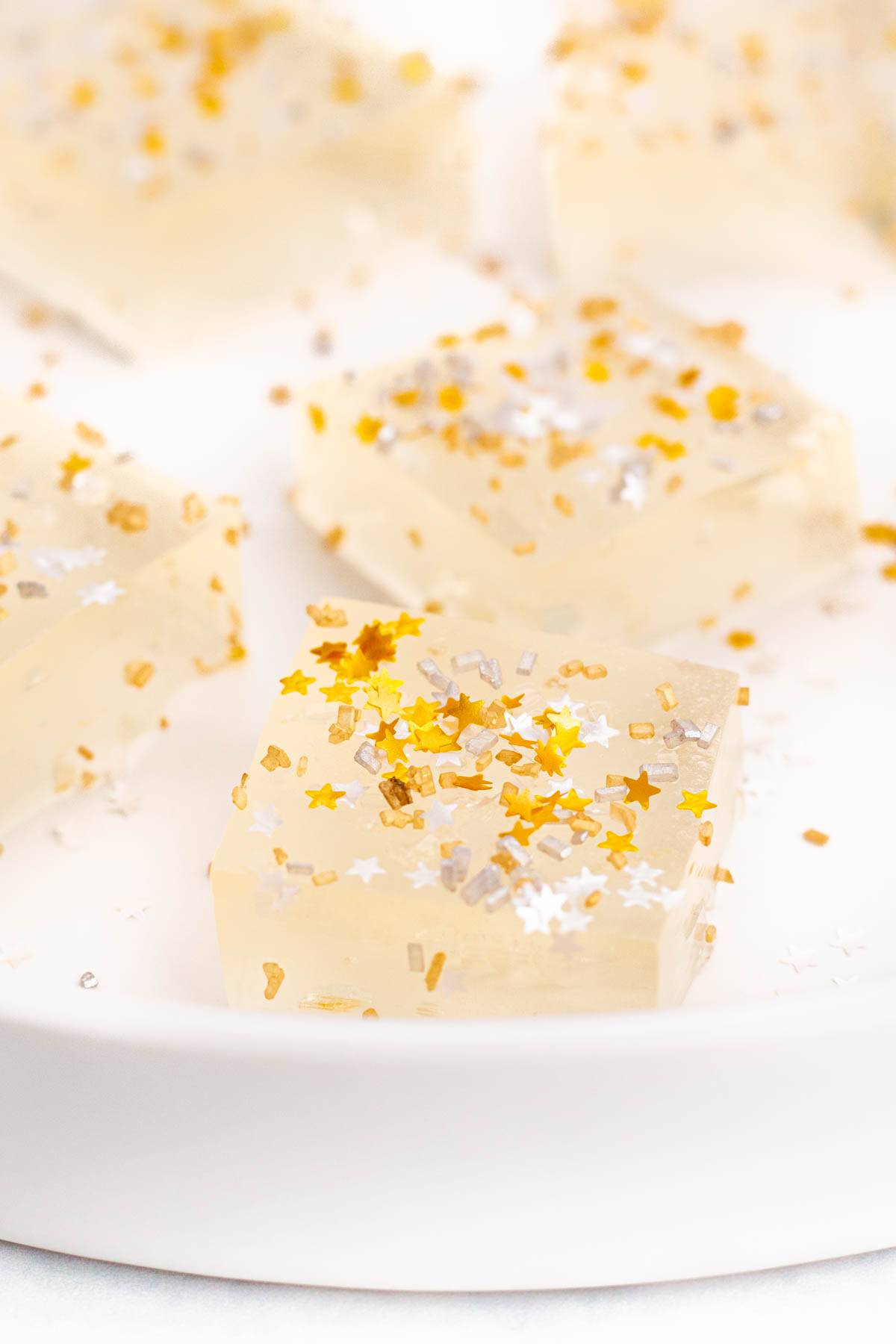 Square jello shots with gold star sprinkles sit on a white plate.