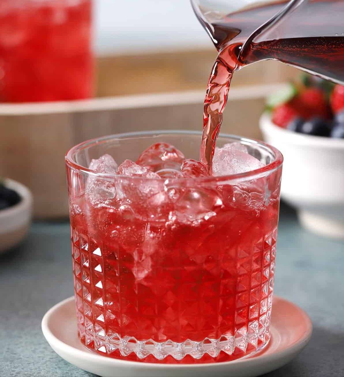 A red drink pours over ice from a pitcher.