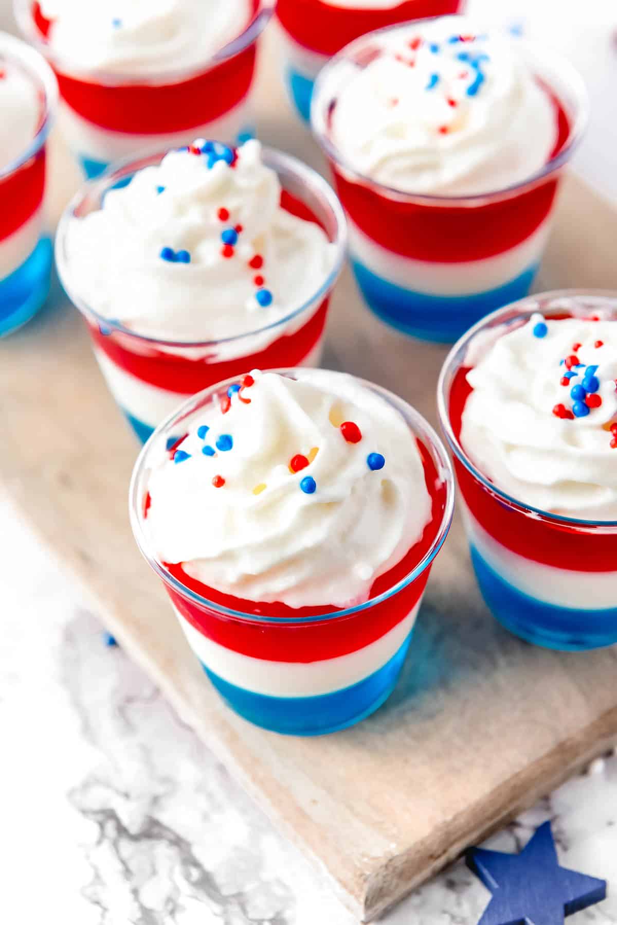 Layered red, white and blue jello shots topped with whipped cream and red and blue sprinkles.