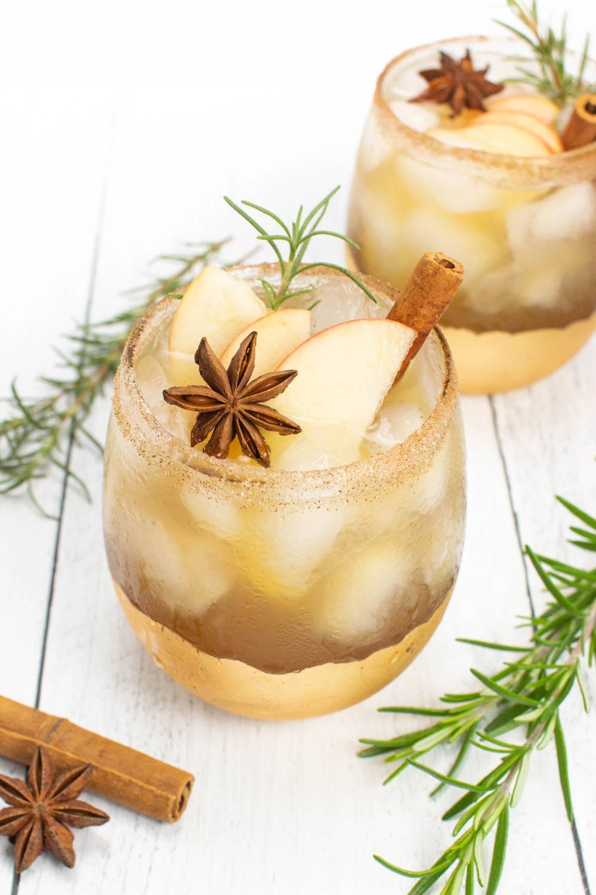 Two glasses of apple cider sangria garnished with apple slices and spices.