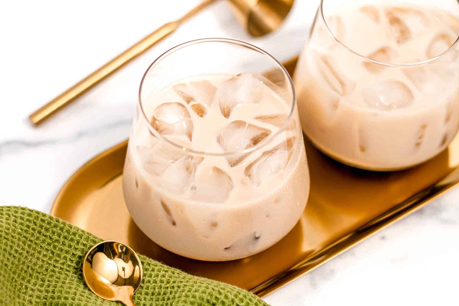 A gold tray holds two creamy iced drinks near gold bar tools.