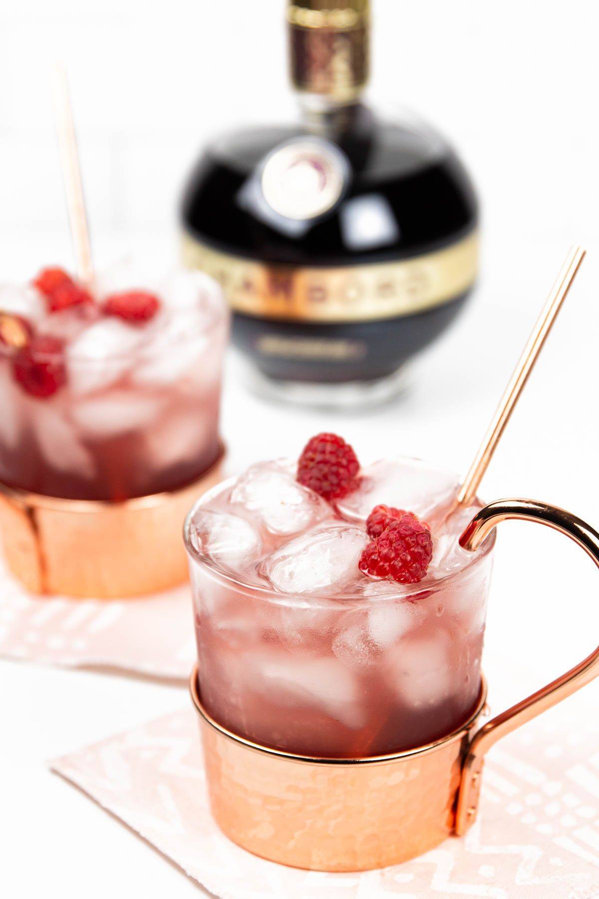 A pink drink in a copper and glass mug with raspberries on top.