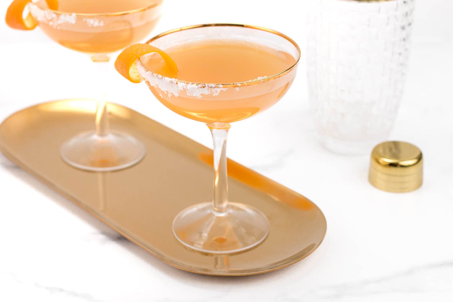 Two stemmed glasses hold orange cocktails on a oval tray.