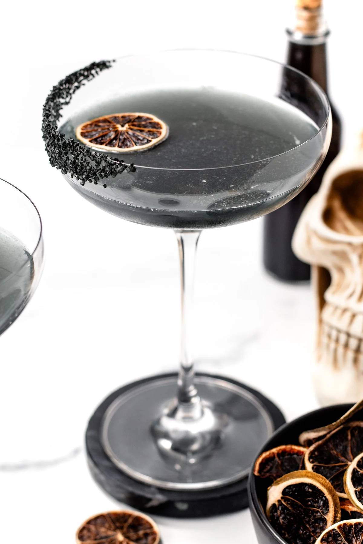 A black margarita in a stemmed glass with a dried orange round floating on the top.