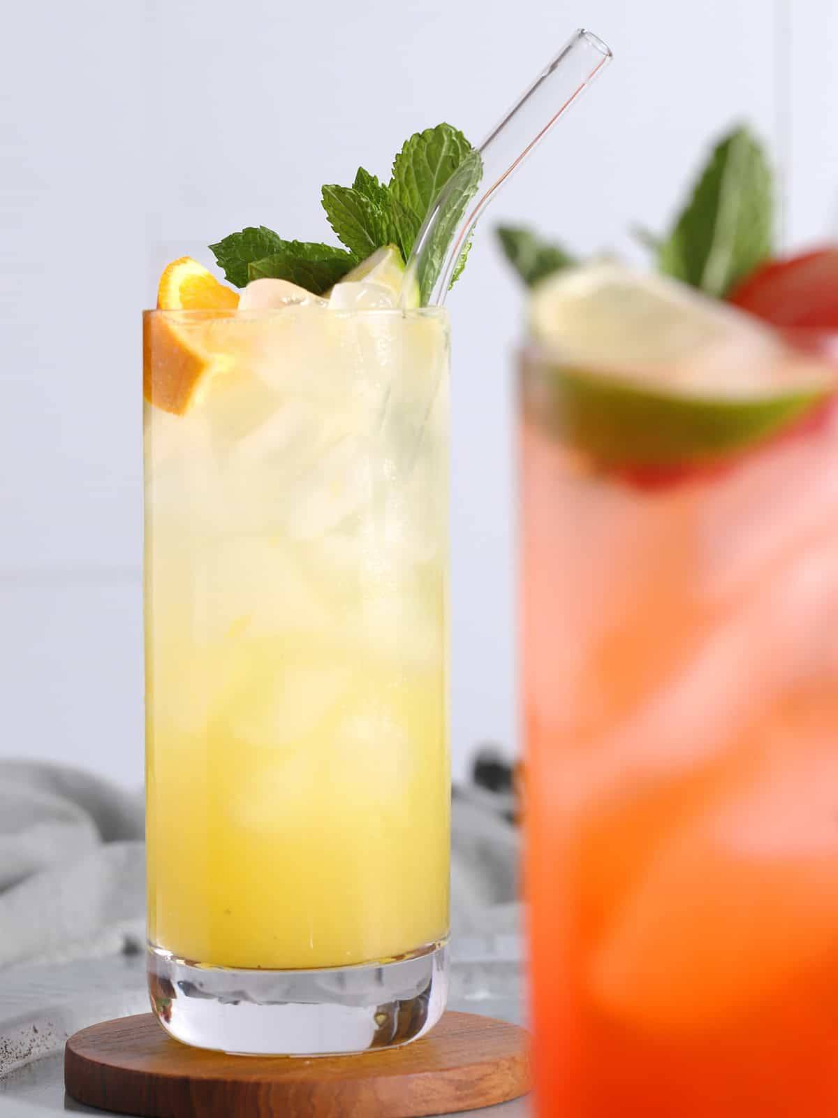 Two tall glasses hold a pale pink drink and a pale orange drink.