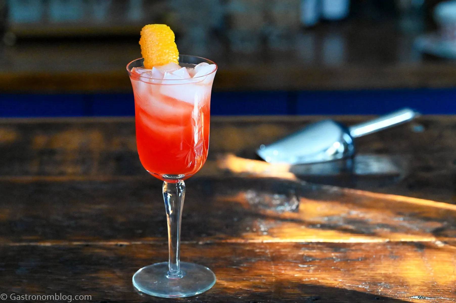 A red drink in a stemmed glass sits on a wooden surface.