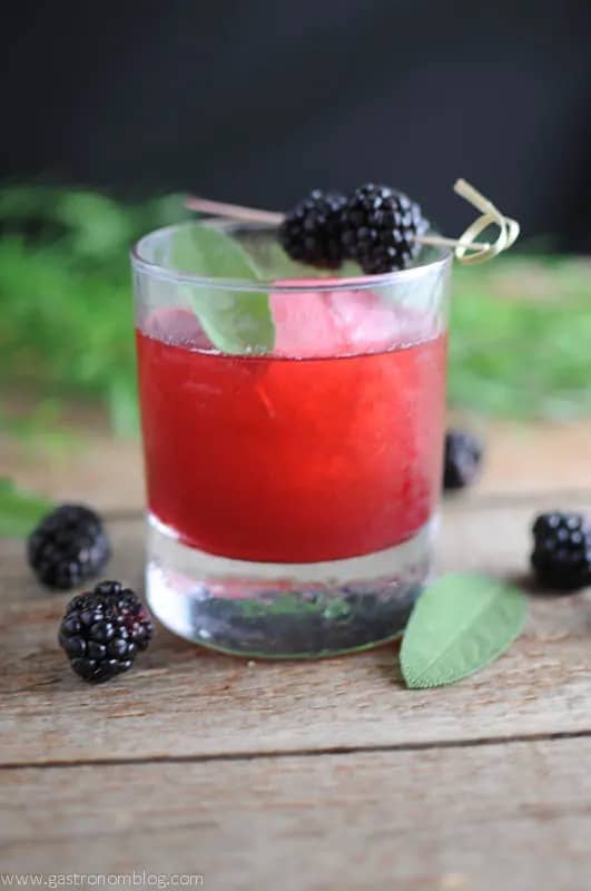 A deep pink drink topped with blackberries on a cocktail skewer.