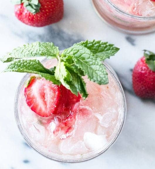 Overhead view of a pink cocktail garnished with mint and strawberry slices.