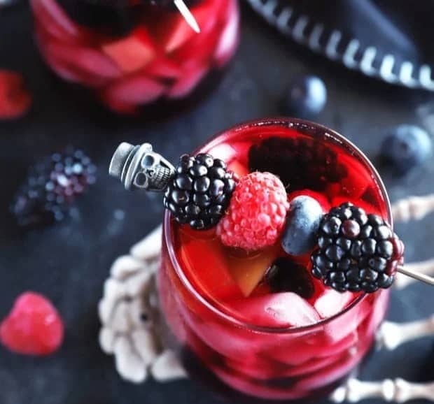 Overhead view of a red berry drink with a skeleton skewer holding berries across the top of the glass.
