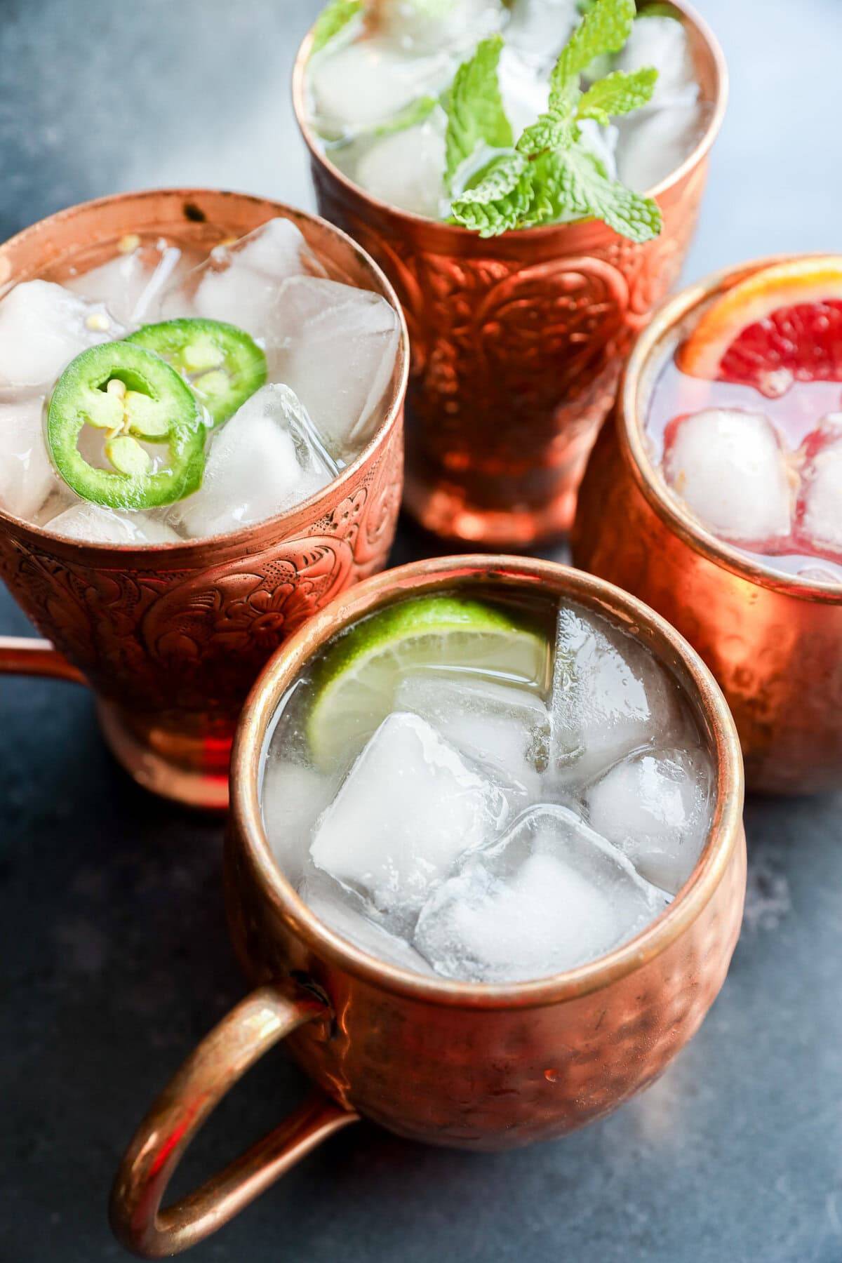 Overhead view of drinks in copper mugs with various garnishees like jalapeño slices, lime and grapefruit.