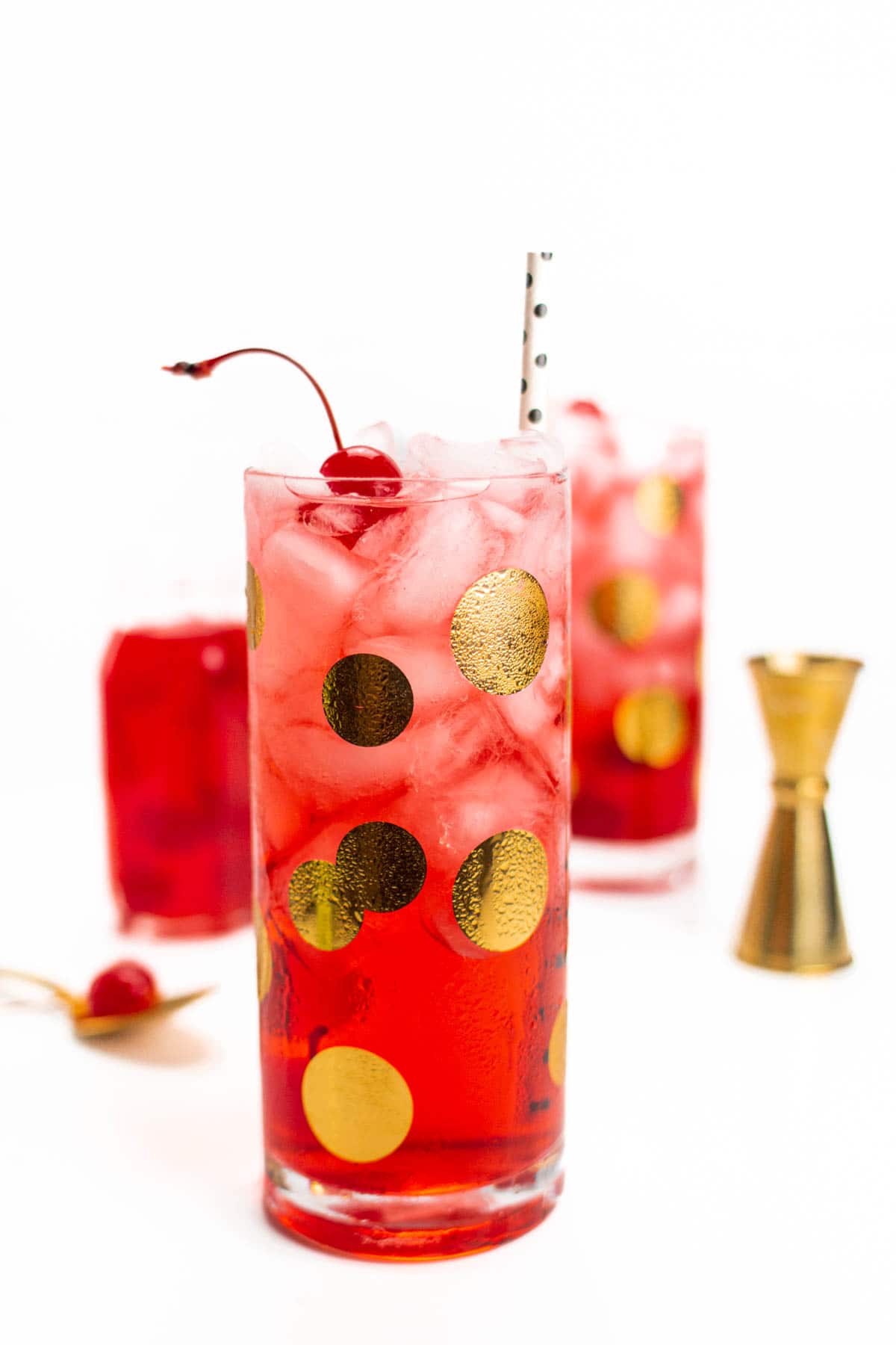 A red drink in a glass with gold polka dots topped with a cherry.
