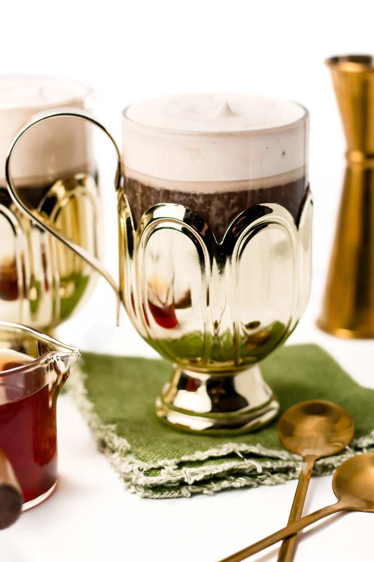 A glass mug holds a creamy coffee drink on a green fabric coaster.