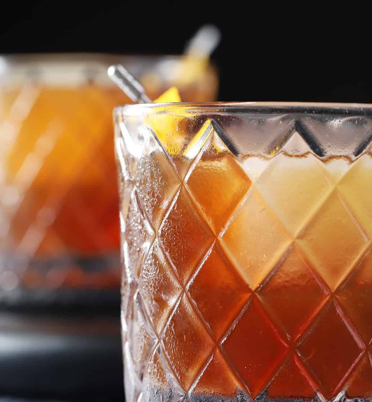 A brown drink in a diamond textured glass with a large ice cube.