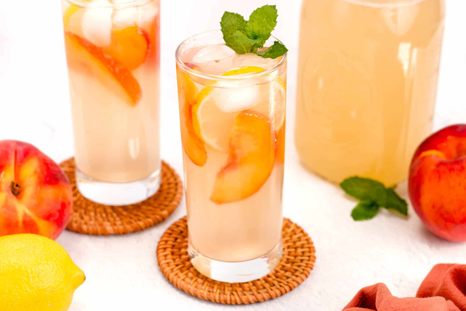 Pale orange drinks in tall glasses with peach slices and ice.
