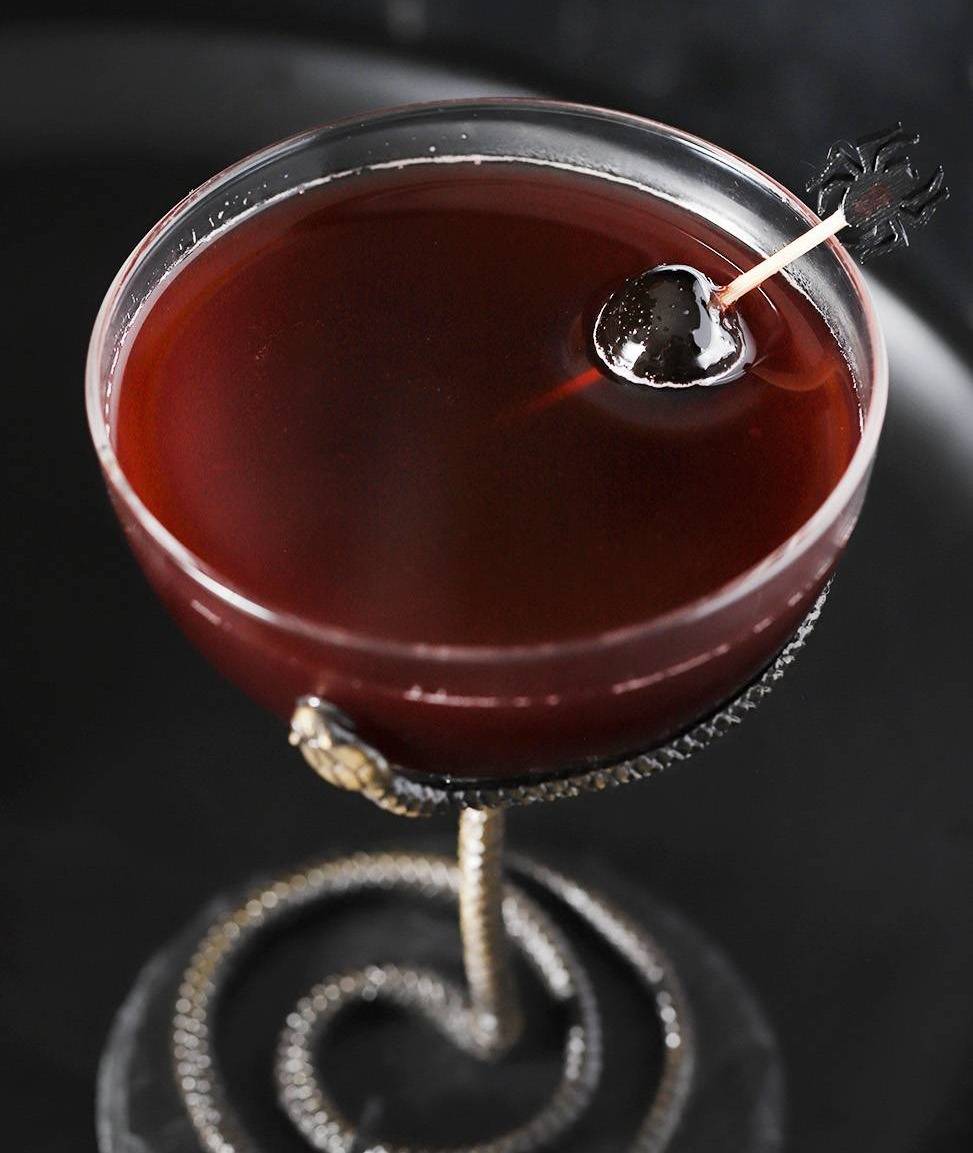 A deep red drink in a glass with a silver snake as the stem.