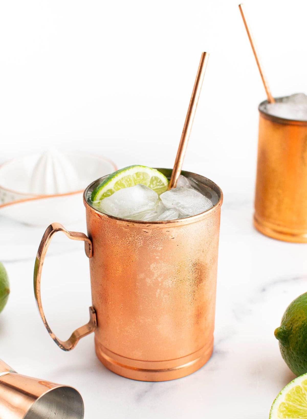Two copper mugs with copper straws filled with a cocktail, ice and lime wedge.