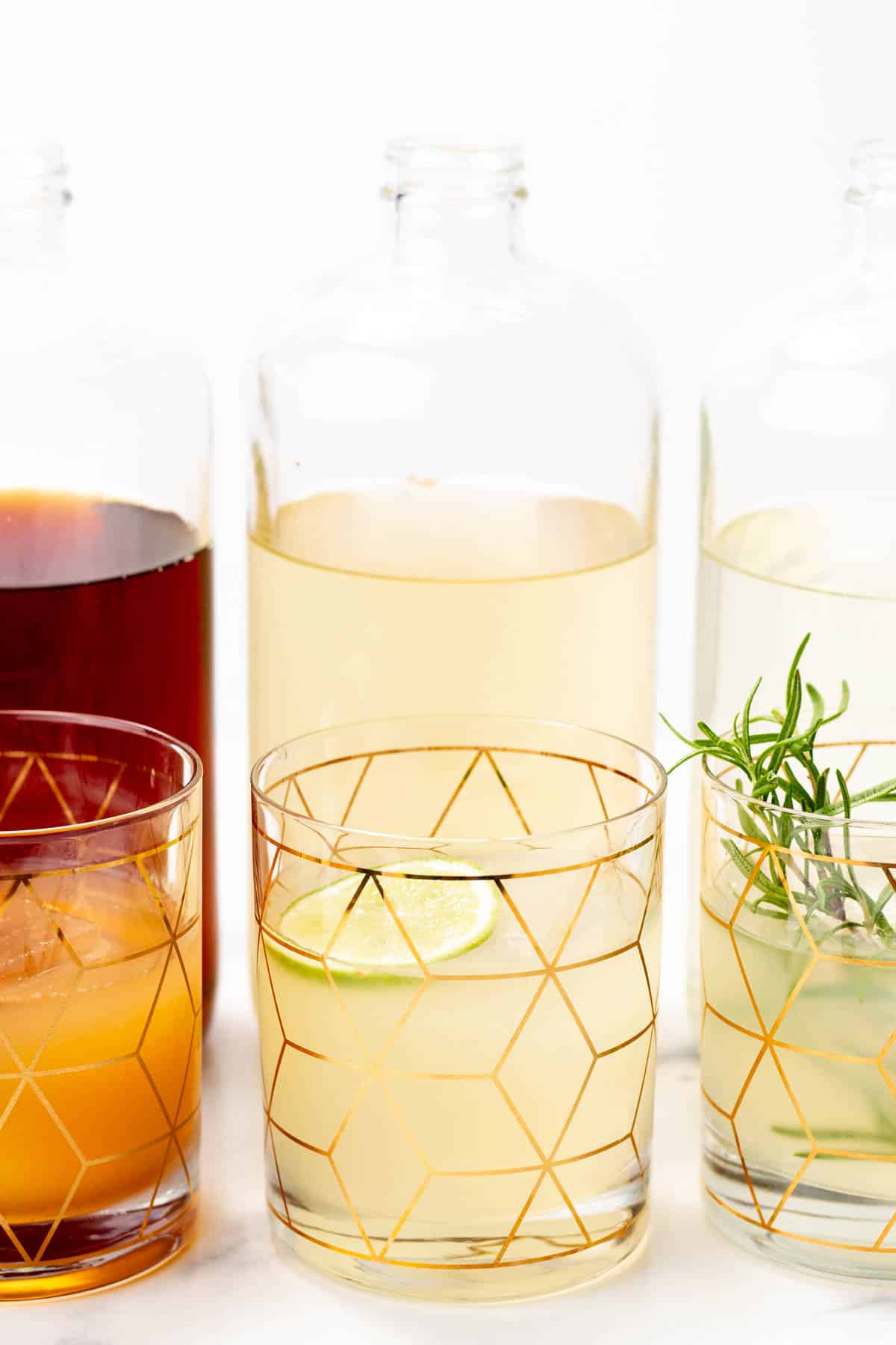 Three glasses with a gold geometric pattern hold drinks in front of bottles of homemade zero-proof spirits.