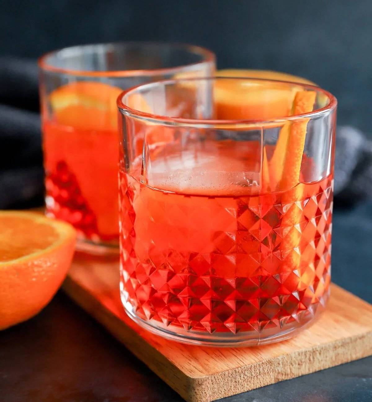 Two red cocktails on a board with orange slices and large ice cubes.