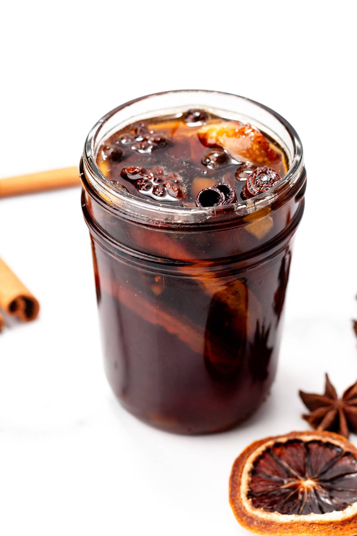 A dark brown simple syrup sits in a jar filled with whole spices.