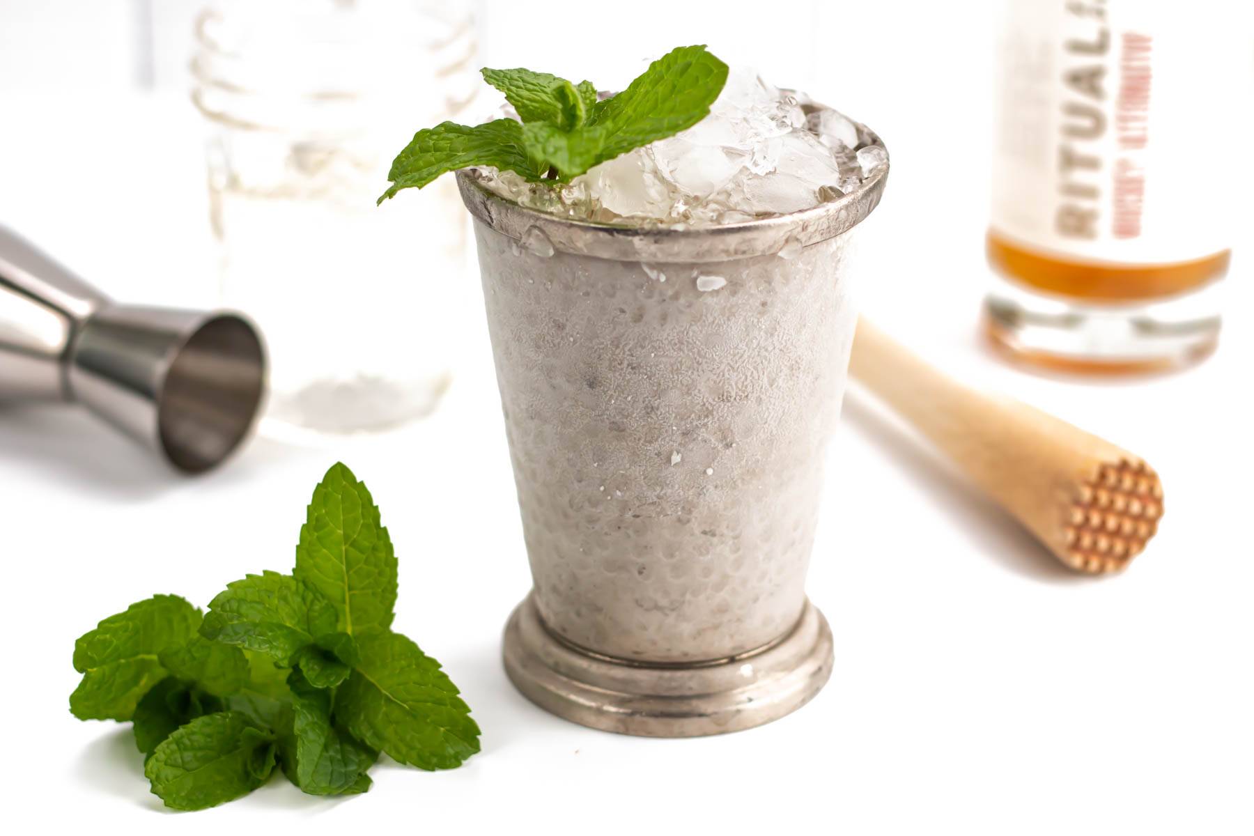 A silver julep cup holds a cocktail made with crushed ice and a sprig of mint.