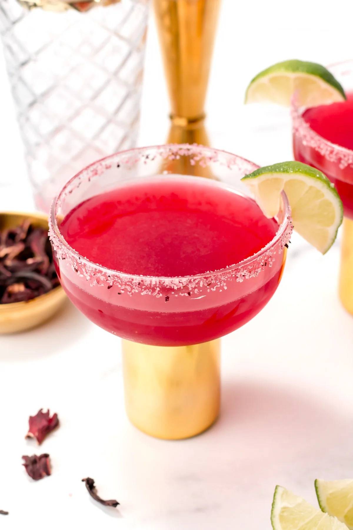 A deep red margarita in a glass with a gold stem with a lime wedge on the edge.