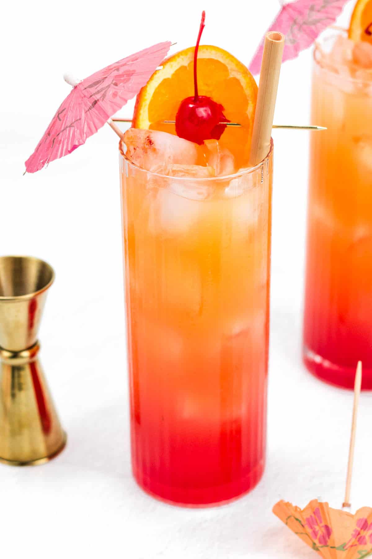 A drink that fades from red to orange garnished with fruit and a cocktail umbrella.