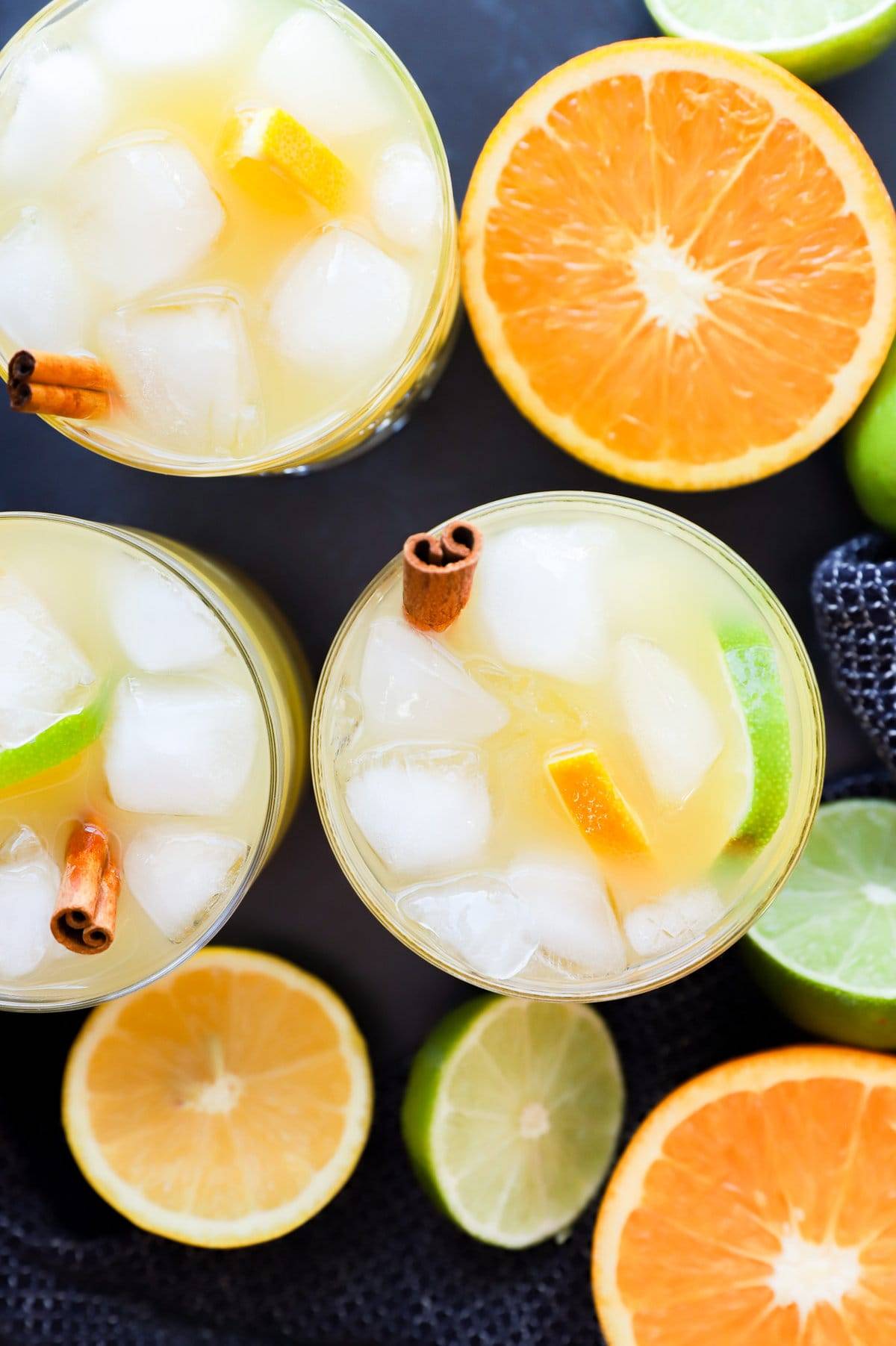 Overhead view of pale yellow drinks with fruit slices near halved oranges and limes.