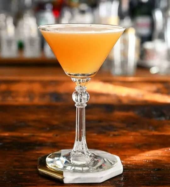 An orange cocktail in a vintage martini glass sitting on a bar counter. 