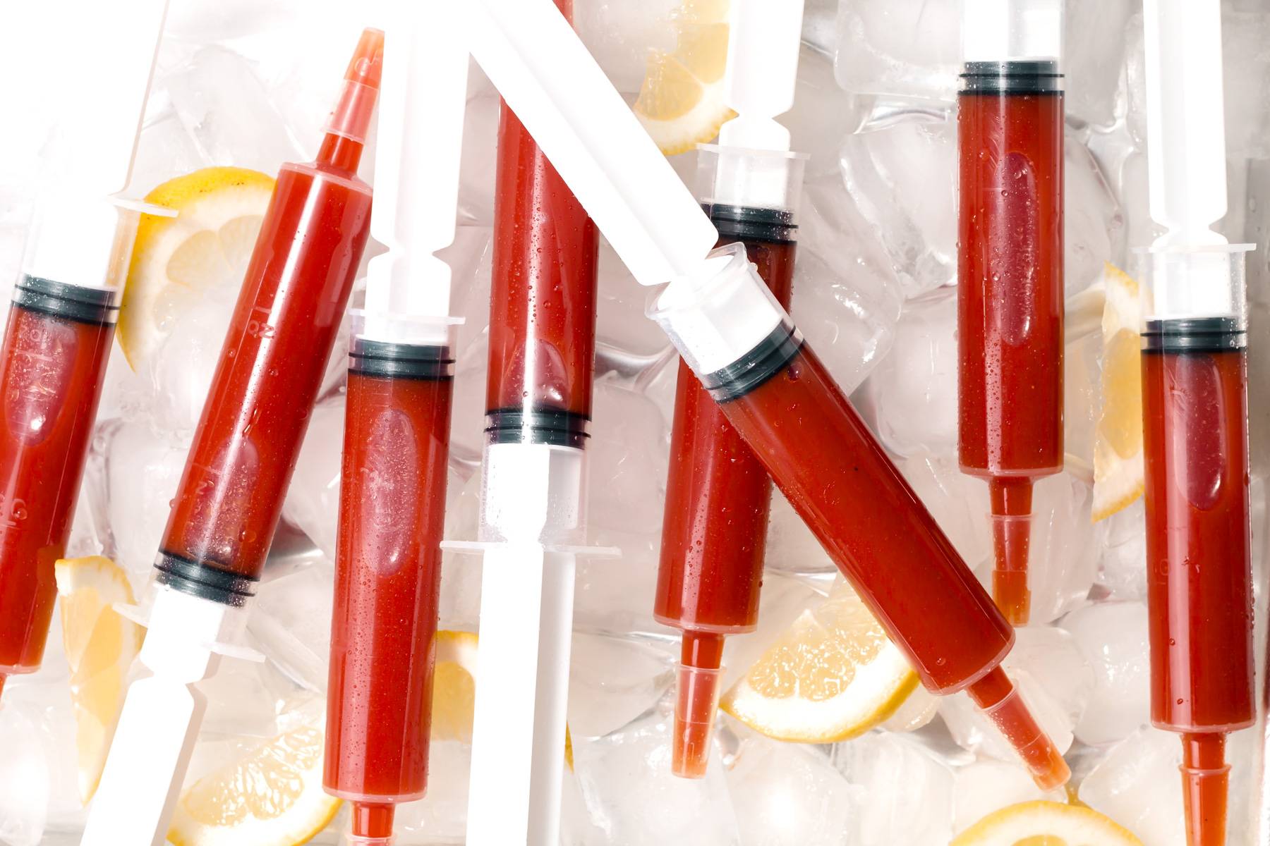 Syringes filled with a red liquid sit on a bed of ice alongside lemon wedges.