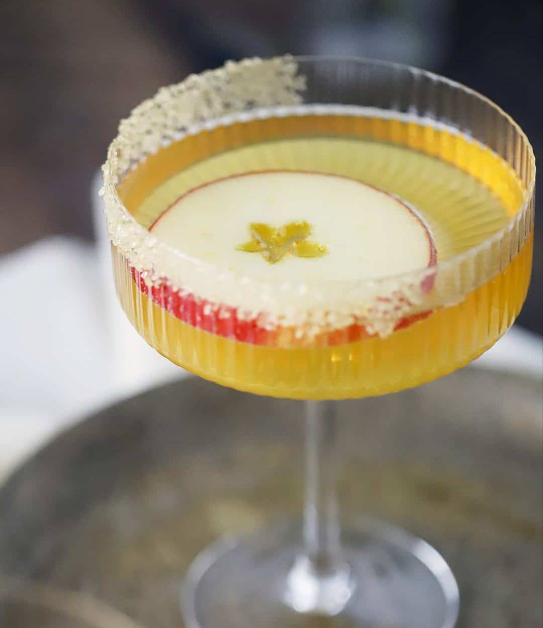 A yellow drink in a stemmed glass with a floating apple round.