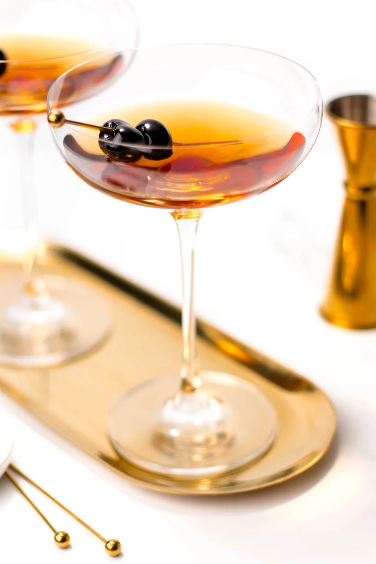 Amber liquid in a coupe glass sits on a gold oval tray.