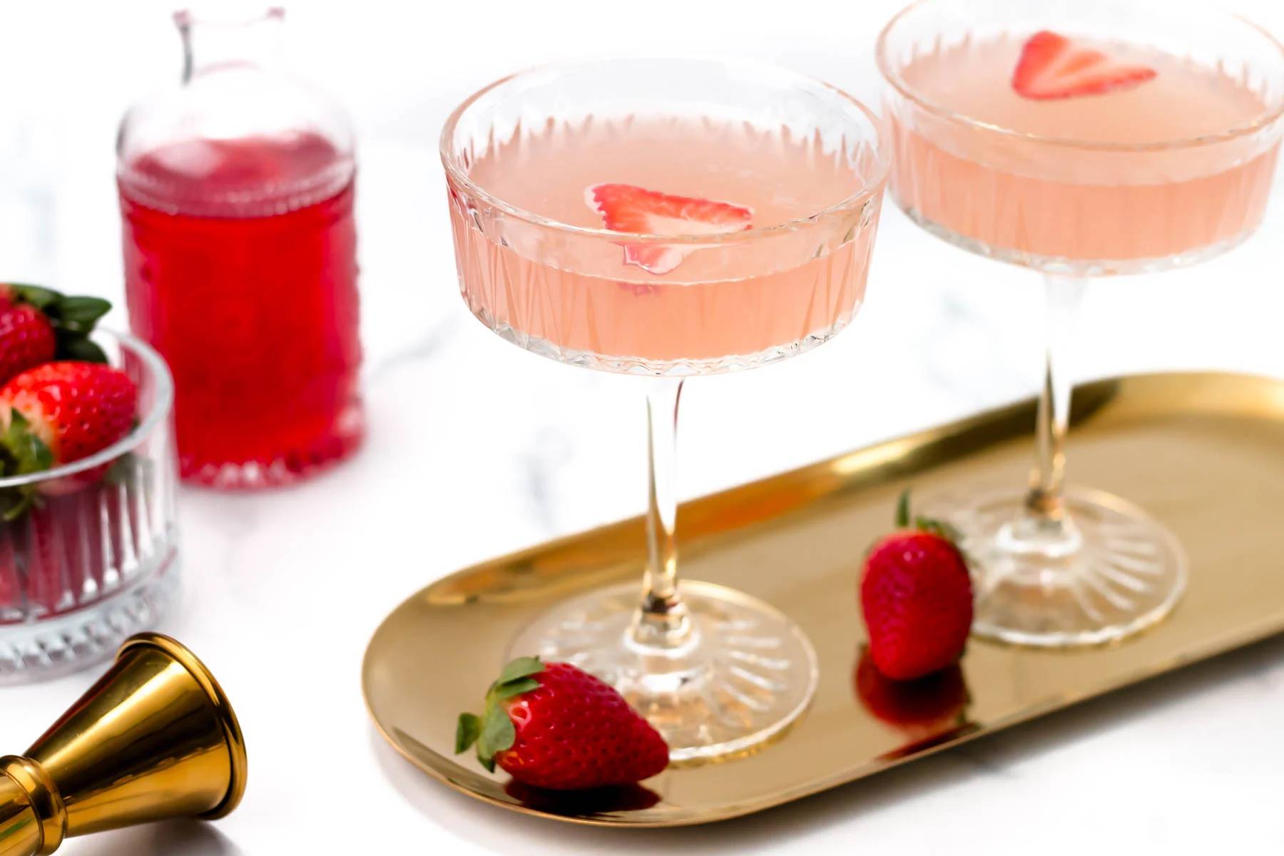 Two pink drinks sit on a gold oval tray.