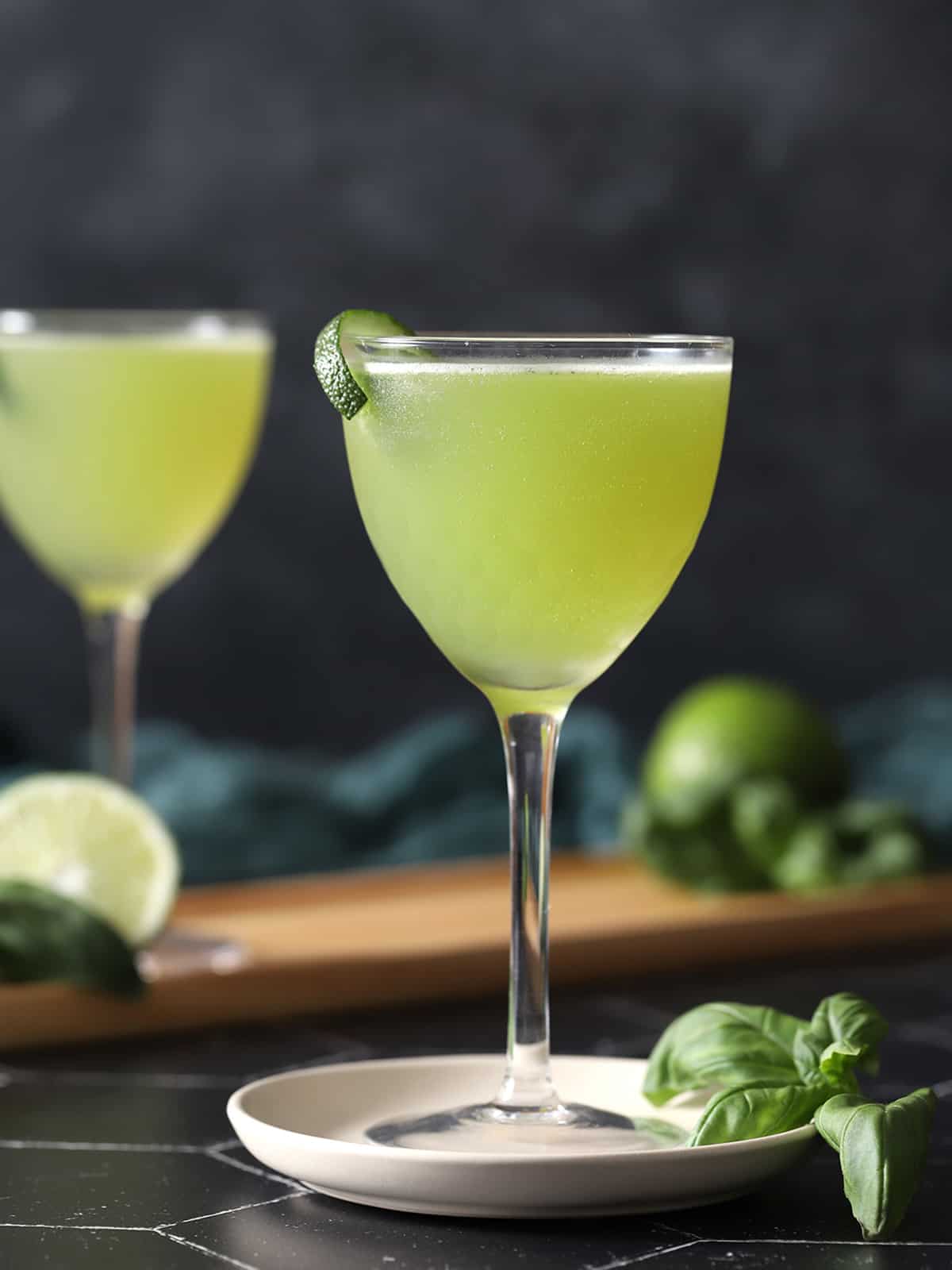 A pale green cocktail sits on a white coaster with a lime wedge on the rim.