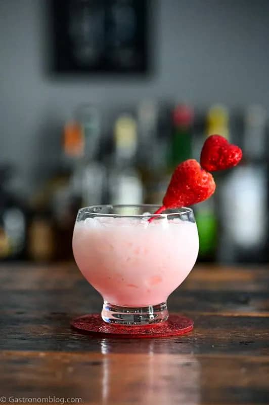 A frothy pink drink garnished with a heart skewer.