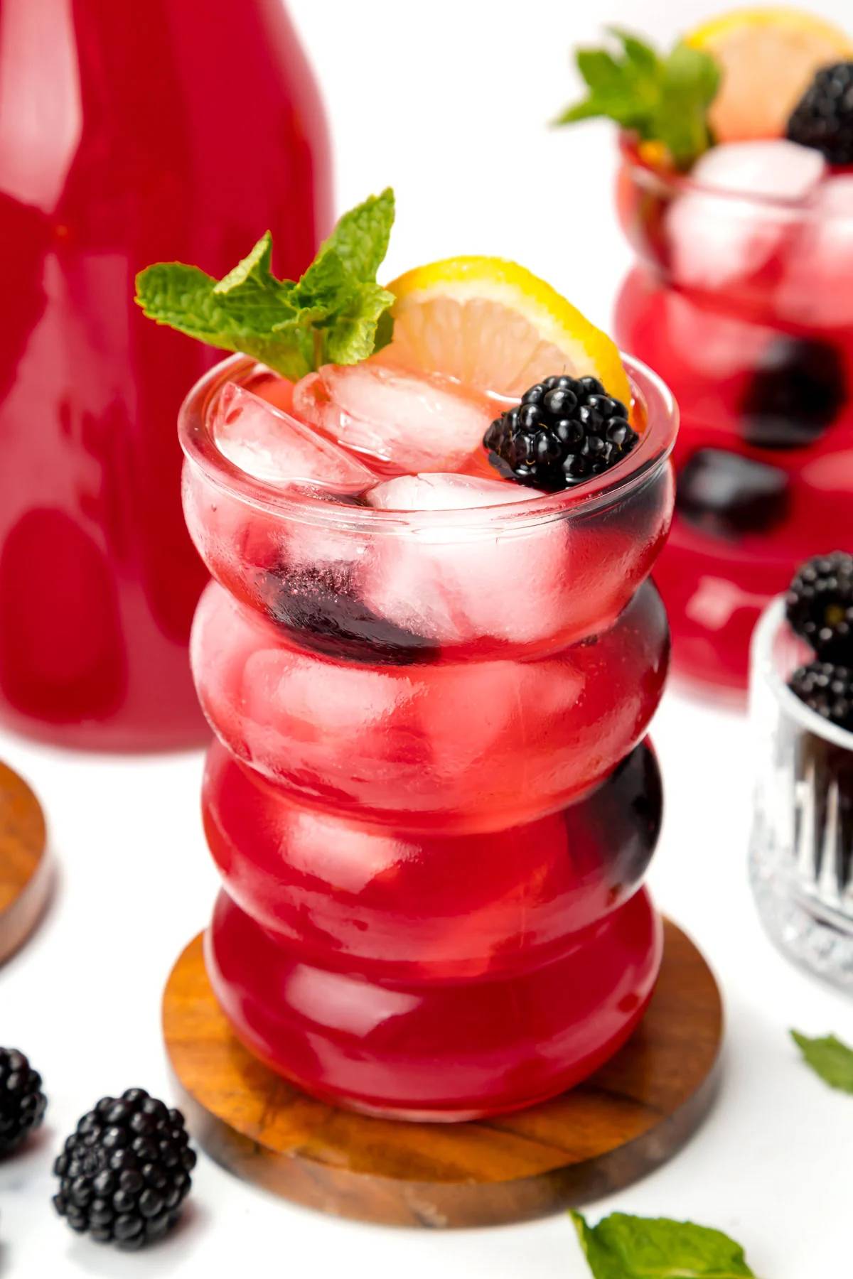 A glass of deep red lemonade with whole blackberries and a lemon slice.