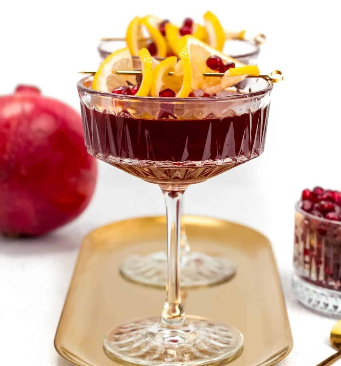 A deep red cocktail garnished with lemons and cranberries.