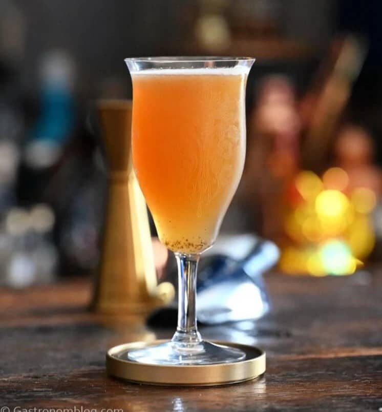 A stemmed glass holding an amber liquid sits on a wooden surface.