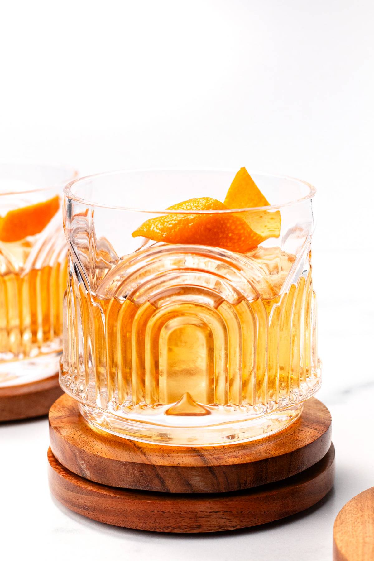A rocks glass with a pale orange drink topped with an orange peel.