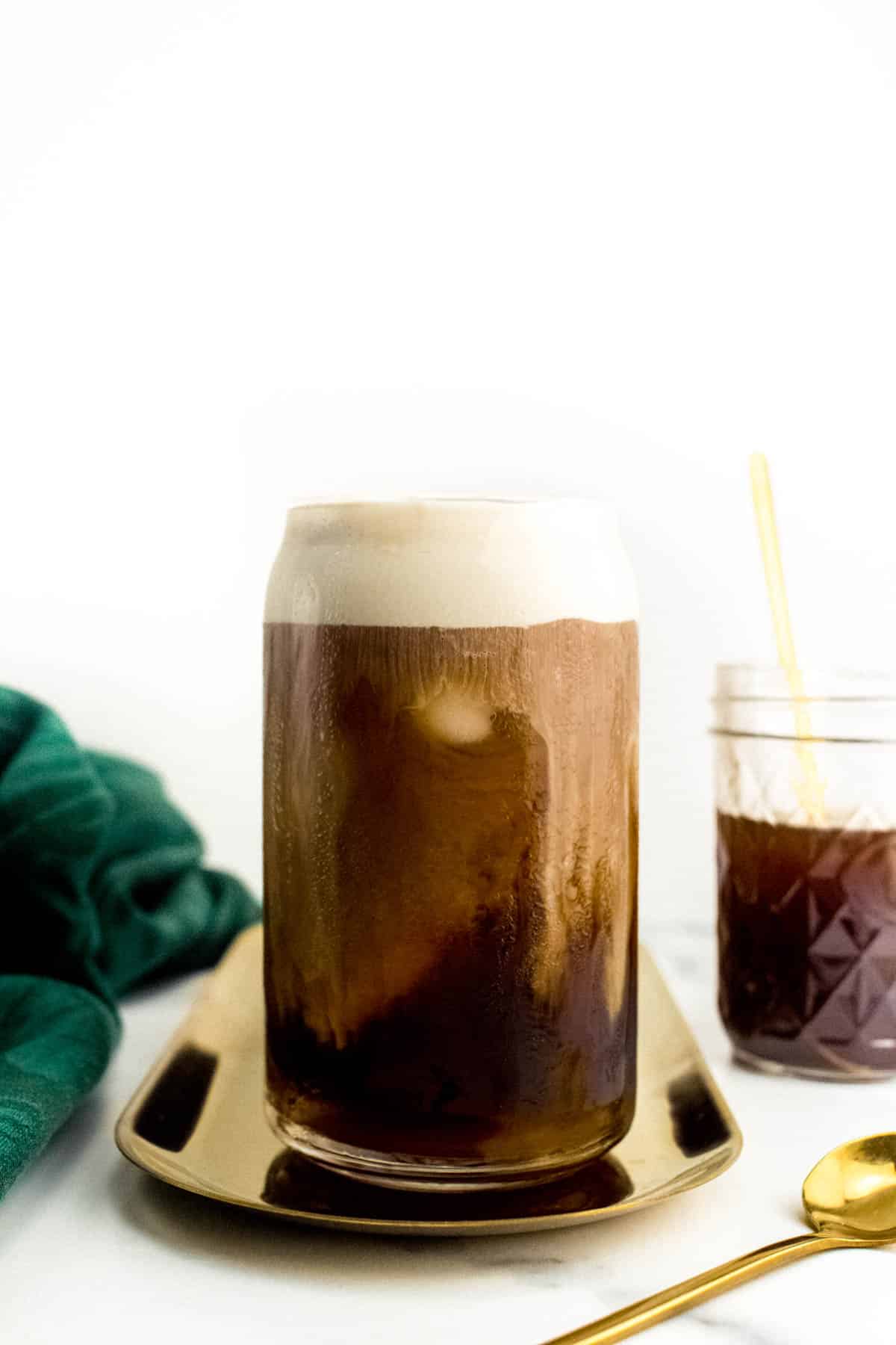 A can glass holds a coffee drink topped with cold foam.