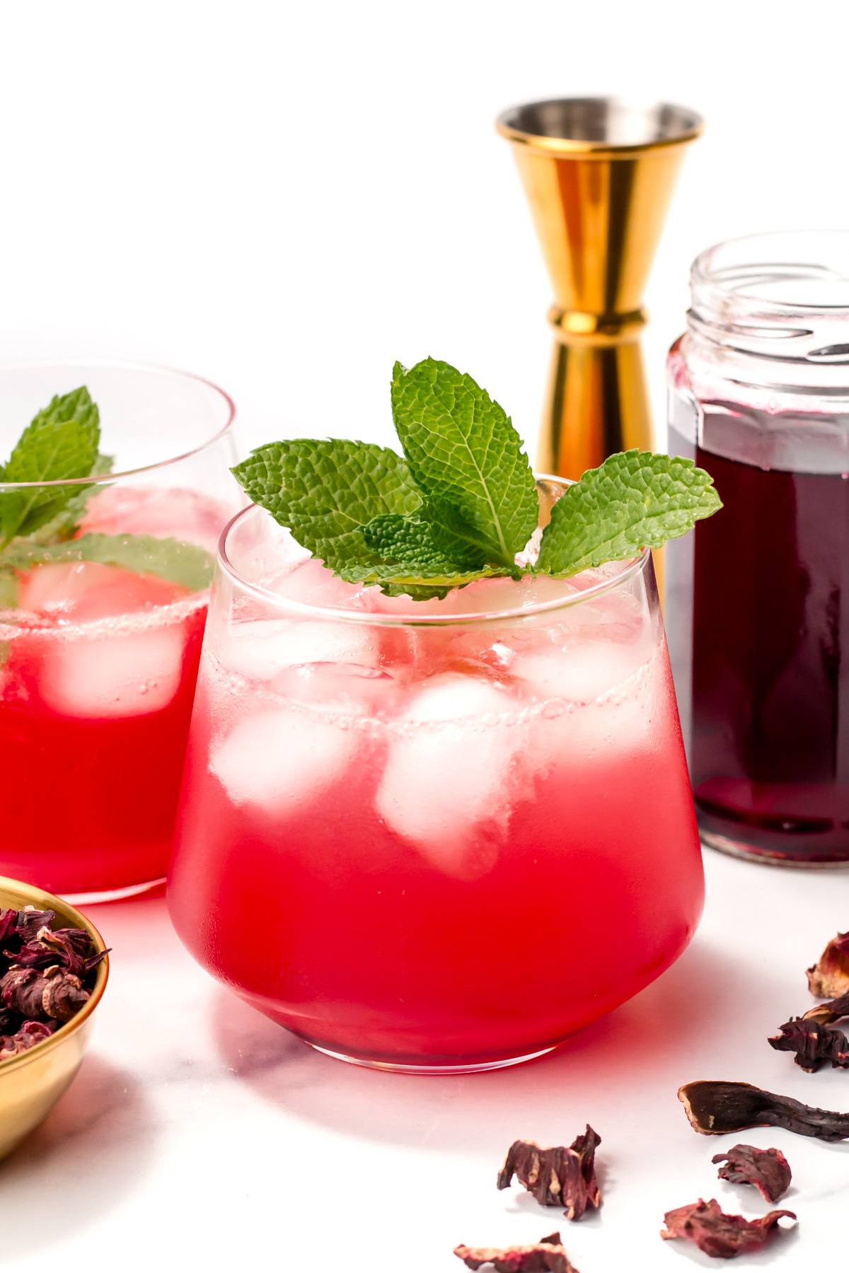 A pink drink with ice garnished with a sprig of herbs.