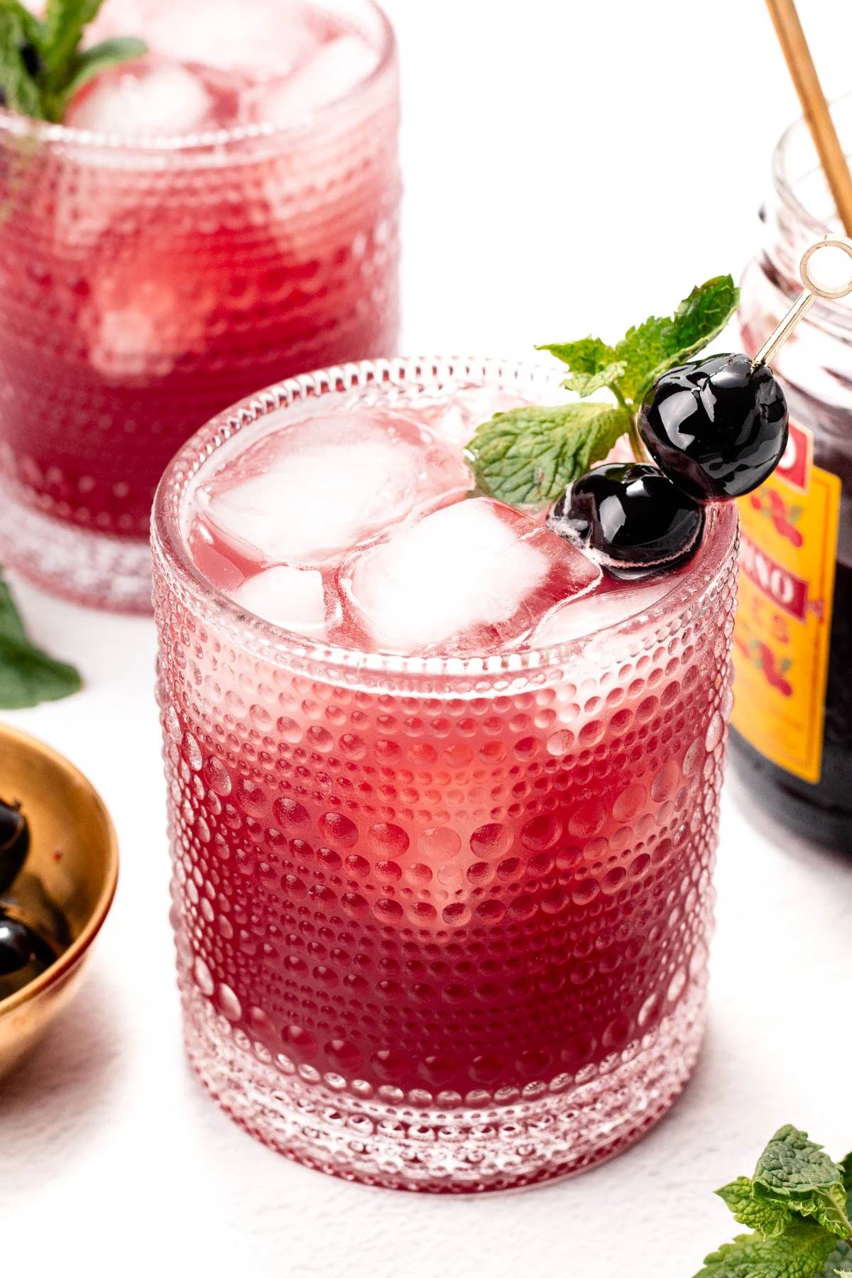 A red drink garnished with cherries on a cocktail pick.