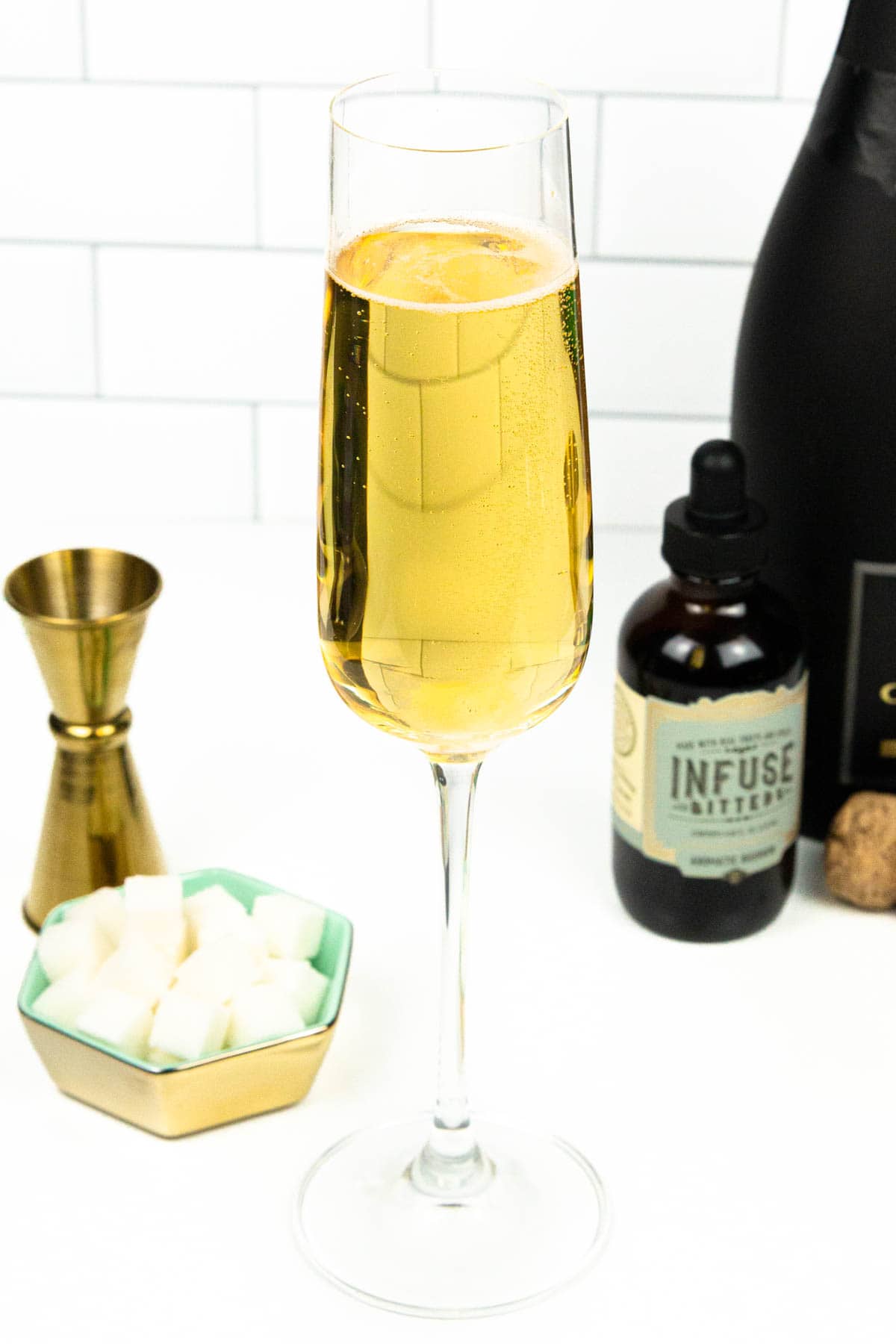 A bubbling glass of champagne in a flute near a bowl of sugar cubes and a bottle of bitters.