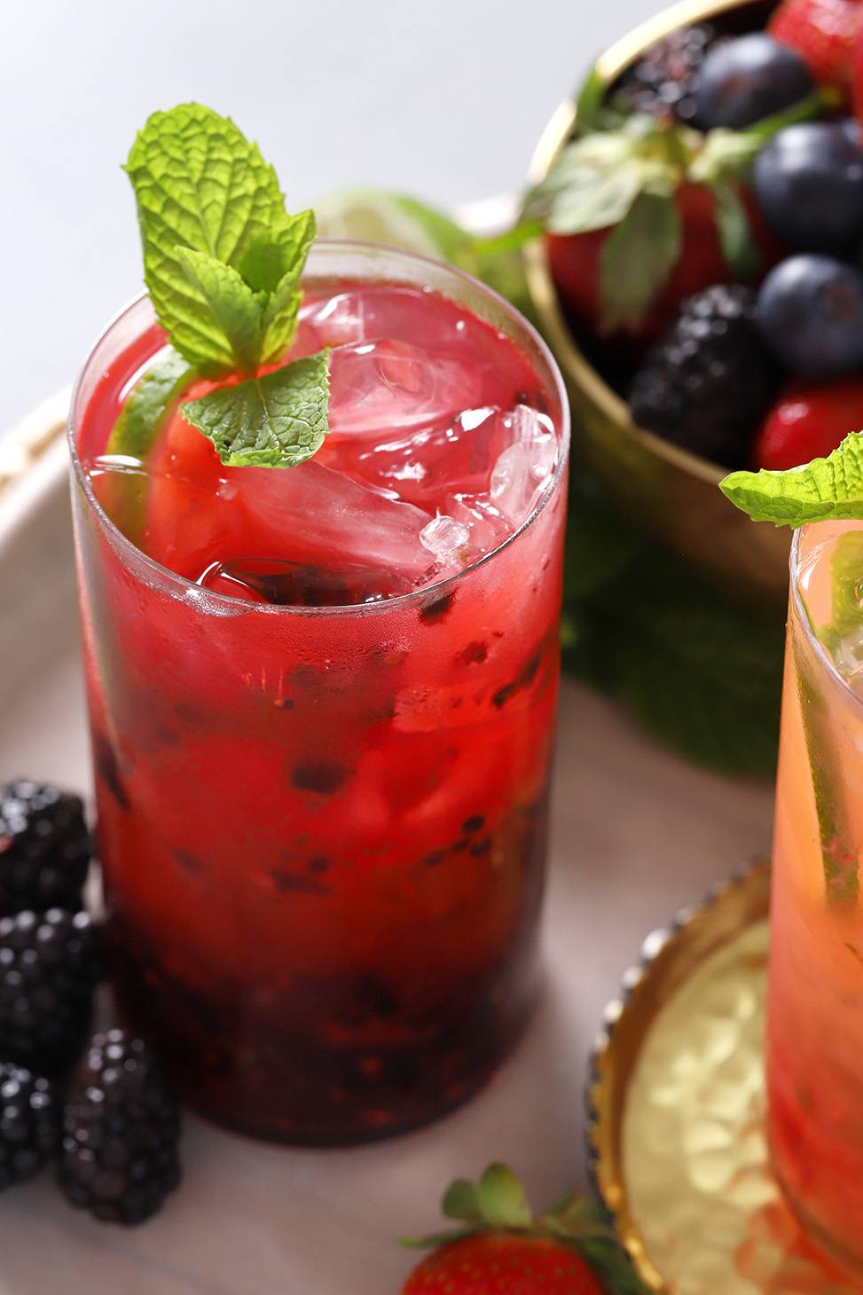 A deep red drink topped with an her sprig near a bowl of berries.
