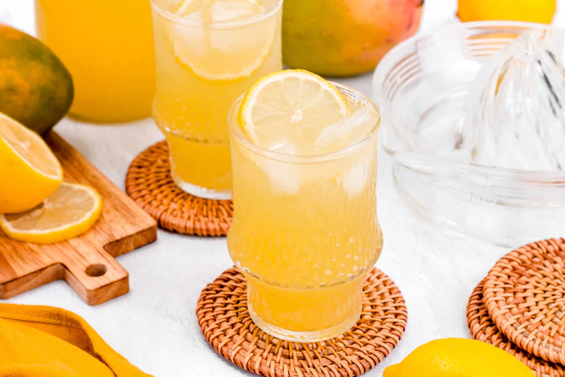 A dark yellow lemonade sits in a glass on a round rattan coaster.