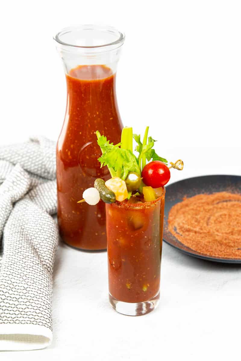 A bloody mary sits in front of a pitcher of bloody mary mix.